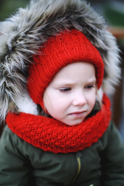 Ritratto di una bambina triste e carina in abiti caldi e capispalla all'aperto da sola con tempo freddo