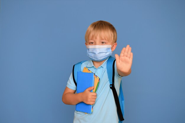 Portrait of a cute schoolboy boy 6 years old with a bright backpack on a blue background. Back to school.