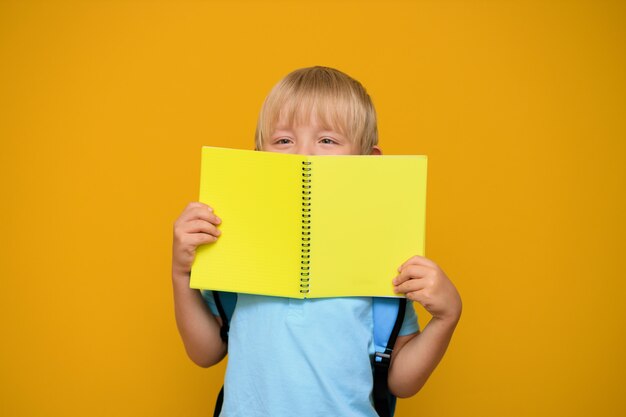 Portrait of a cute schoolboy boy 6 years old with a bright backpack on a yellow background. back to school