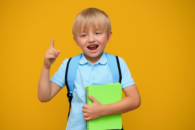 黄色の背景に明るいバックパックで6歳のかわいい少年のポートレート。学校に戻る。