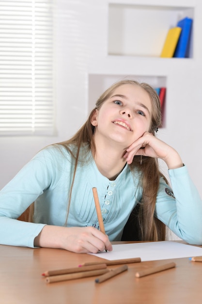 Portrait of cute schoolgirl sitting at table and drawing