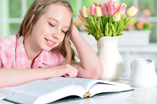 Portrait of cute schoolgirl sitting at table and reading