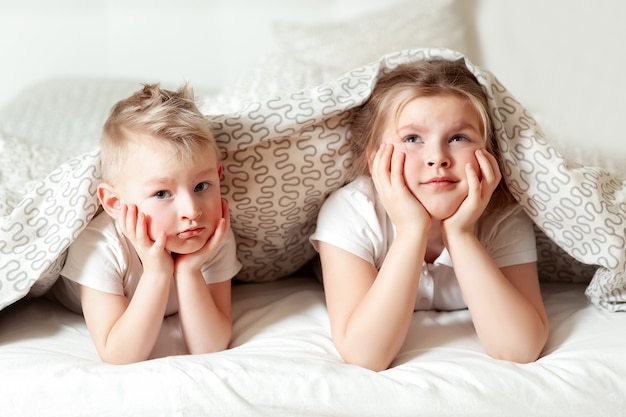 Portrait of cute siblings under blanket in bed