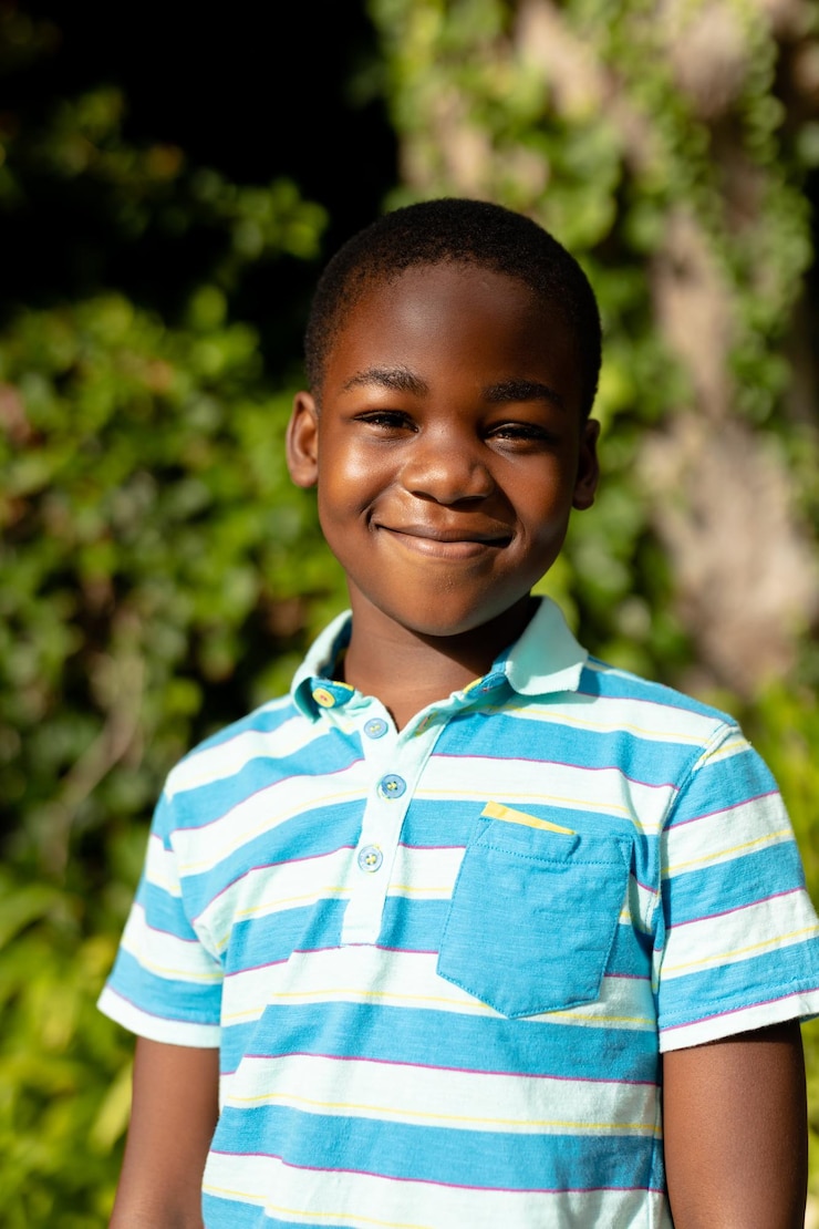 Photo portrait of cute smiling african american boy standing against plants outdoors