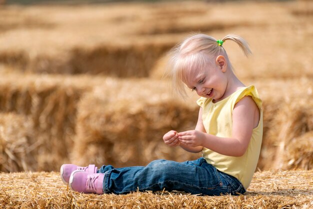 Portrait of cute smiling girl on haystack. Childhood on the farm. Hay harvesting.