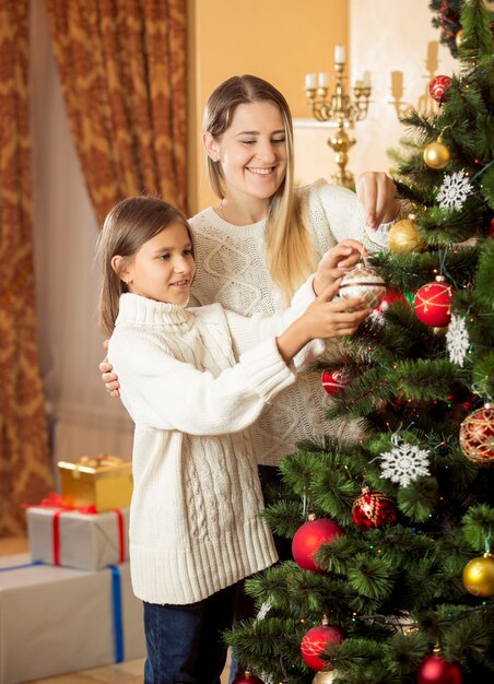 Portrait of cute smiling girl helping mother decorating Christmas tree