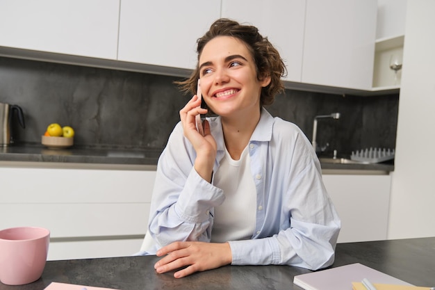 Portrait of cute smiling girl talks on mobile phone sits at home and calls someone with smartphone