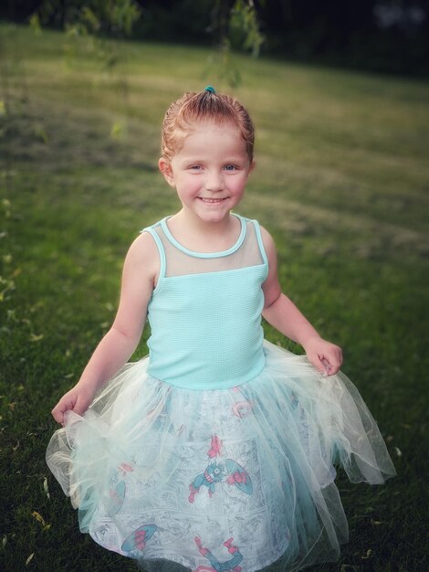 Photo portrait of cute smiling girl wearing blue dress while standing on field