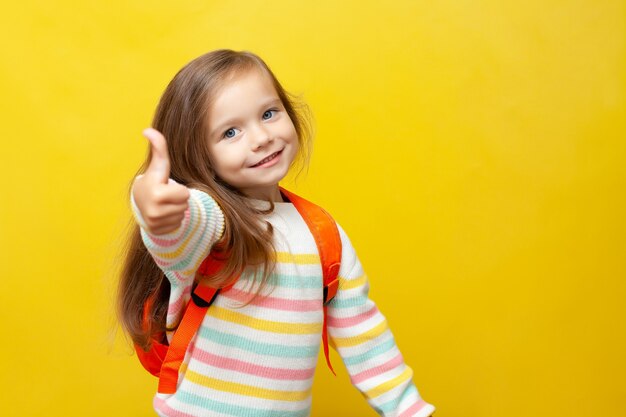 Portrait of a cute smiling girl with a backpack European Back to school Thumbs up