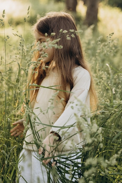 portrait of a cute smiling girl with beautiful hair posing for a photo in the middle of tall grass in a coniferous forest at sunset