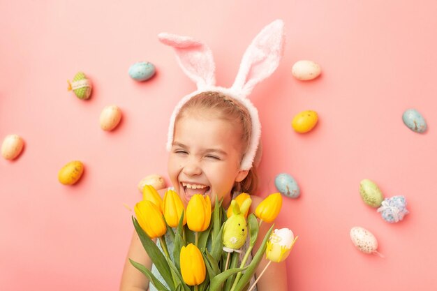 Photo portrait of cute smiling girl with bunny ears and easter eggs holds spring bouquet of tulips