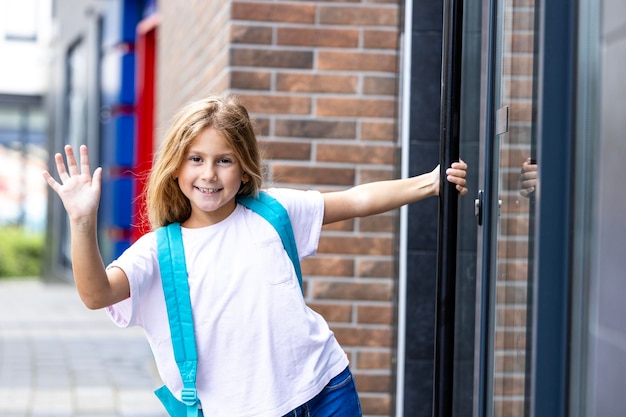 Photo portrait of cute smiling girl with schoolbag entering school building back to school