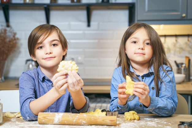 Photo portrait of cute smiling kids boy and girl making cookies from dough in the kitchen