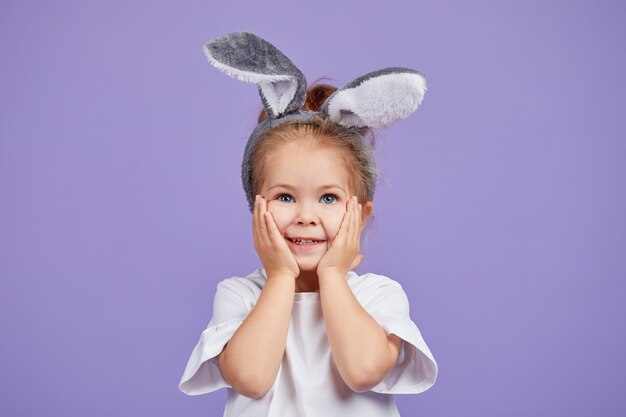 Portrait of cute smiling little child girl wears bunny ears on Easter day. Funny emotions on Violet isolated space