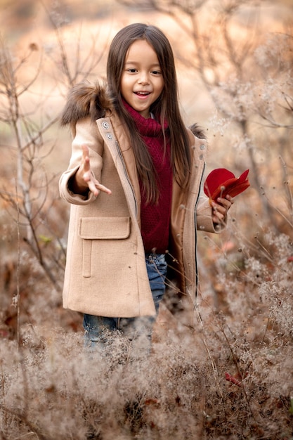 Portrait of cute smiling little girl playing with autumn fallen leaves