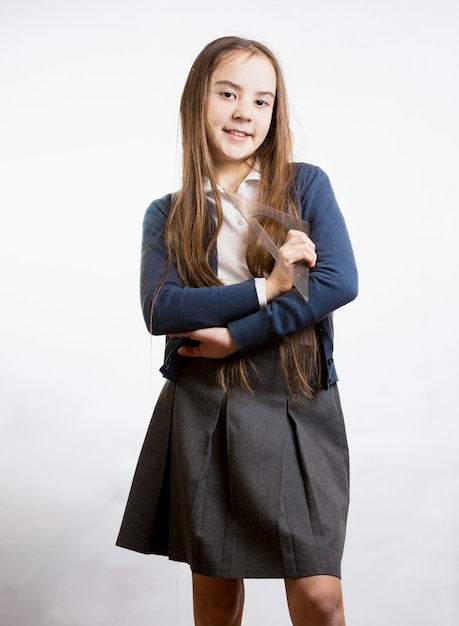 Portrait of cute smiling schoolgirl holding plastic ruler against white background