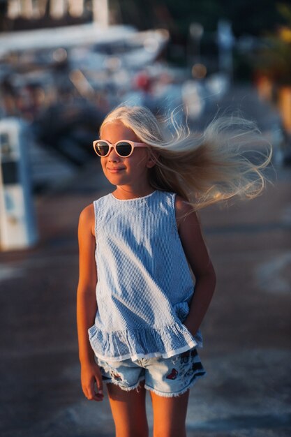 眼鏡をかけたかわいい笑顔の10歳の少女の肖像画。ショートパンツの少女と海の近くの日没時の青いTシャツ。トルコ。