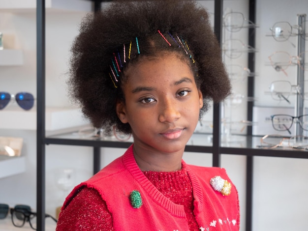 Portrait of a cute teenage African girl with afro hairstyle wearing a red dress is trying on glasses in an optical shop during the Christmas season