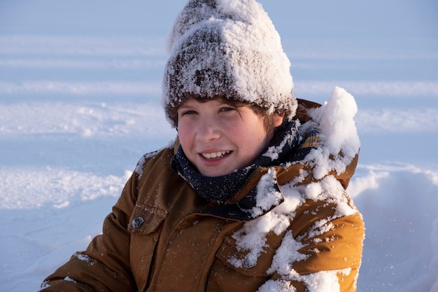 Portrait of a cute teenage boy preteen playing in snow in a snowcovered hat in winter nature