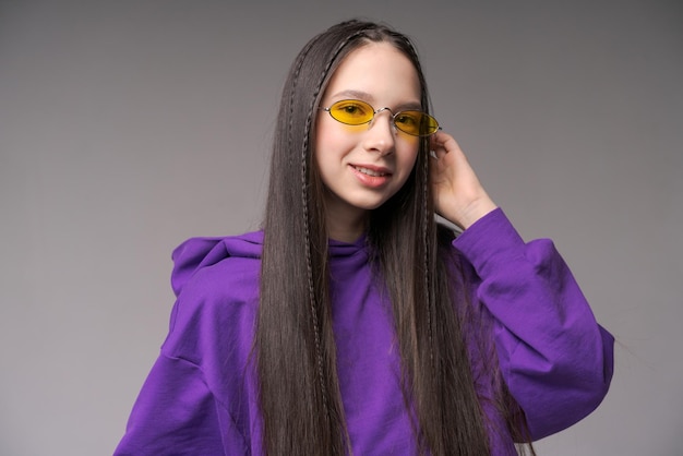 Portrait cute teenage girl in purple sweatshirt and yellow glasses posing