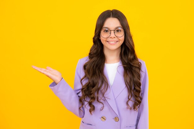 Portrait of cute teenager child girl pointing hand showing adverts with copy space over yellow background