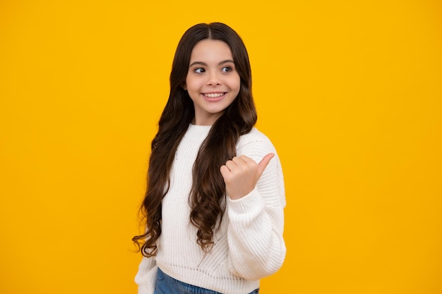 Portrait of cute teenager child girl pointing hand showing adverts with copy space over yellow