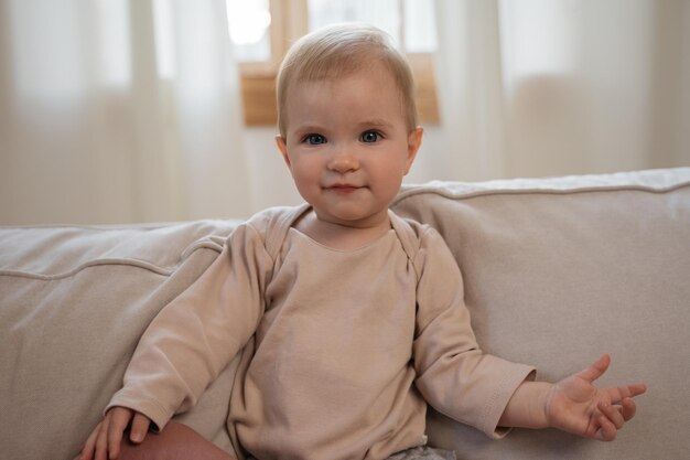 Photo portrait of cute tittle baby looking at camera sitting on sofa