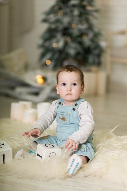 Portrait of a cute toddler playing on the floor near a Christmas tree. 