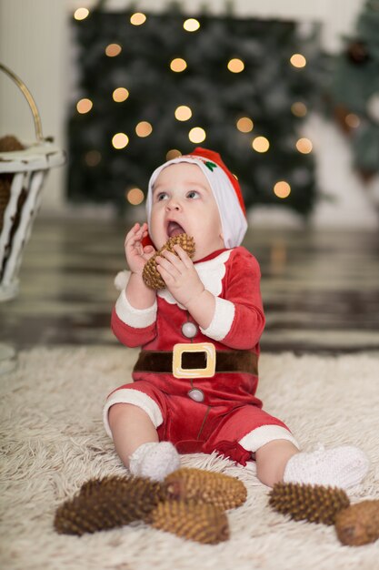 クリスマスツリーを飾るためにコーンで床で遊ぶかわいい幼児の肖像画。