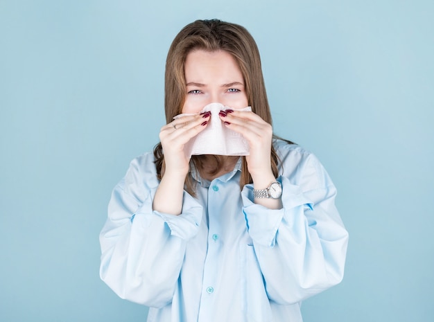 Portrait of cute unhealthy Caucasian female with paper napkin sneezing, experiences allergy symptoms, caught a cold.Sick desperate woman has flu.Rhinitis, cold, sickness, allergy concept