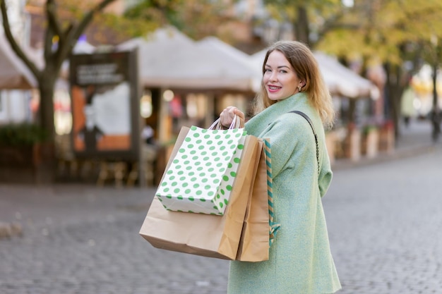 ショッピングバッグ屋外ショッピングコンセプトを持つかわいい広い笑顔の陽気な縮れ毛の女性の肖像画