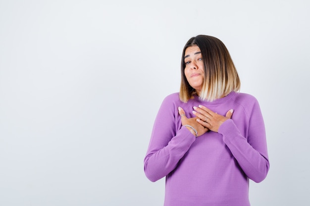 Portrait of cute woman with hands on chest in purple sweater and looking grateful front view