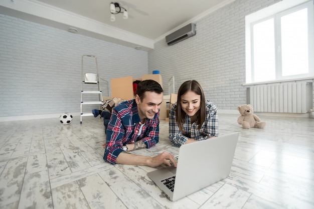 Portrait of a cute young couple lying on the floor at home and managing budget using laptop