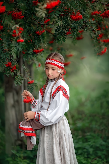 Portrait of a cute young girl in folk dress near a Rowan tree