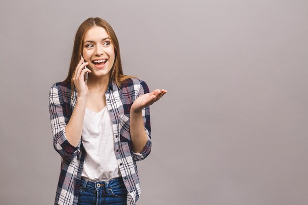 Portrait of cute young joyful woman with trendy hairstyle wearing casual, talking on mobile phone isolated over grey wall.