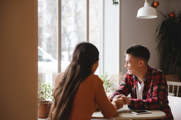 portrait of a cute young loving couple sitting in cafe indoors holding hands of each other.