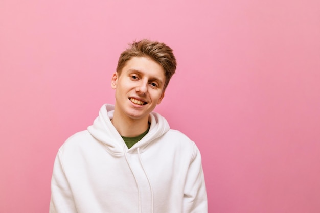 portrait of a cute young man with blond hair and in a white hoodie isolated on a pink background