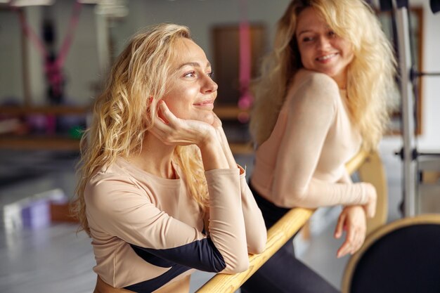 Portrait of cute young woman dancer smiling away while standing near ballet barre together with her friend in stretching studio Healthy lifestyle sports concept