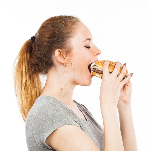 Foto ritratto di una giovane donna carina che mangia un hamburger isolato su bianco