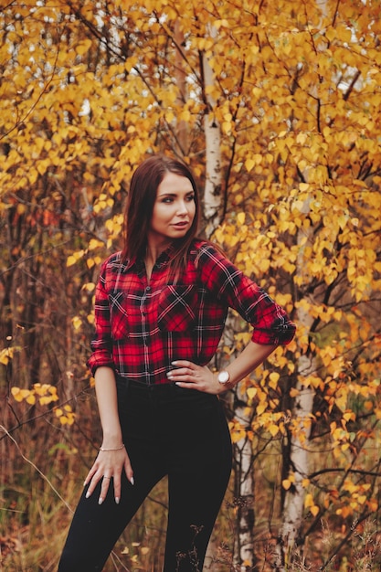 Portrait of cute young woman of Slavic appearance in casual wear in autumn, on countryside against background of an autumn Park. Pretty female walking in forest in golden fall. Copy space