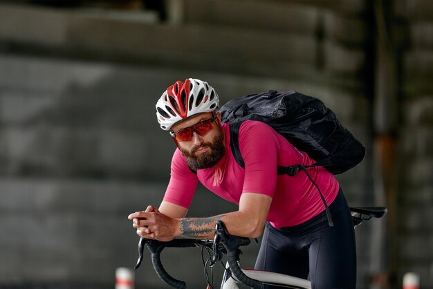 Portrait of a cyclist standing under a bridge with a bicycle in his hand posing at the camera