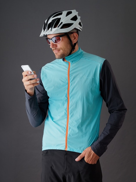 Portrait of cyclist wearing helmet and blue windbreaker, looking at smartphone.