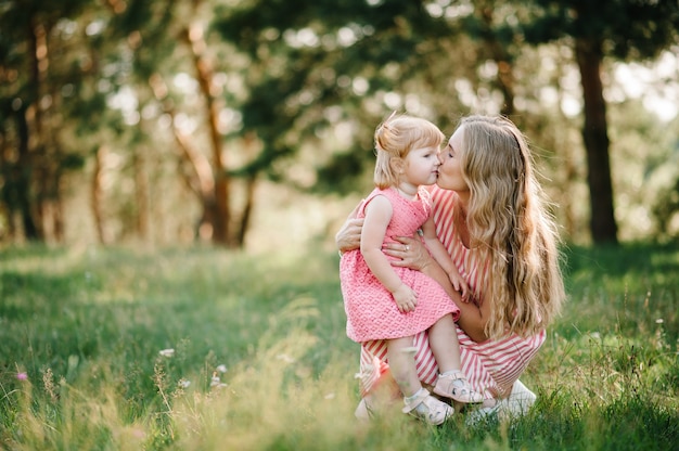 Portrait of a daughter hugging and kissing mother on nature on summer day vacation. Mom and girl playing in the park at the sunset time. Concept of friendly family. Close Up.