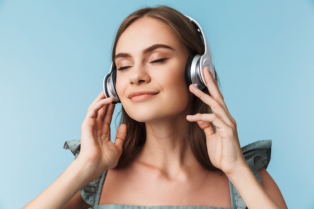 Portrait of a delighted young woman in dress in headphones