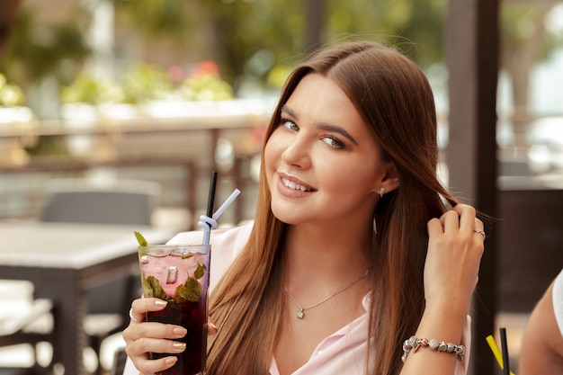 Portrait of delightful young woman holding glass of cold refreshing cocktail