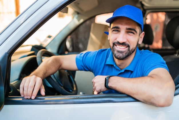 Portrait of a delivery man driver driving van with cardboard boxes on seat