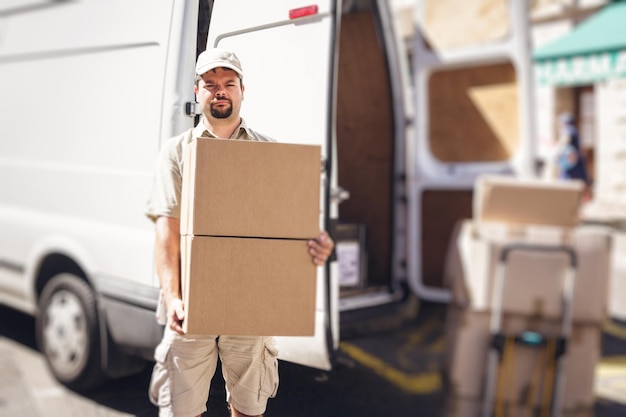 portrait of delivery man holding cardboard boxes while standing by van