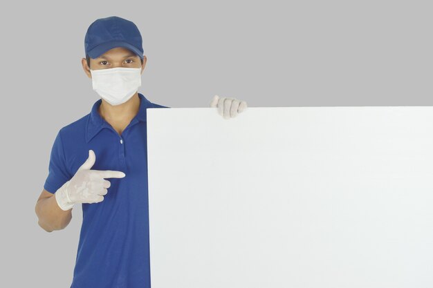 Portrait of delivery man wearing medical mask and medical gloves holding blank billboard on grey