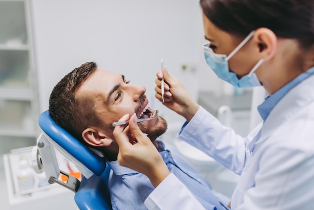 Portrait of dentist in medical mask checking patient teeth with mirror in dental clinic