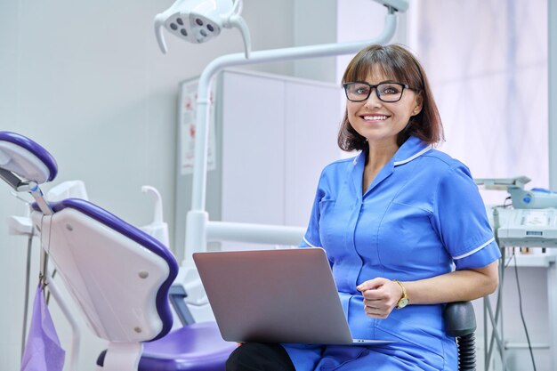 Photo portrait of dentist nurse sitting in office with laptop in her hands looking at camera